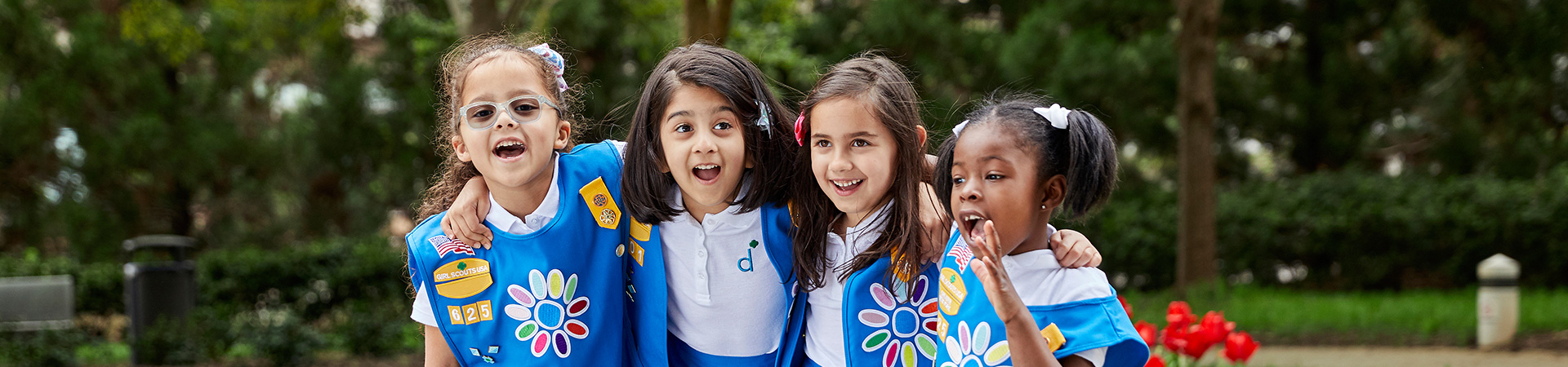  Group of kindergarten Girl Scout Daisies in vest and apron uniform hugging and smiling outside. 