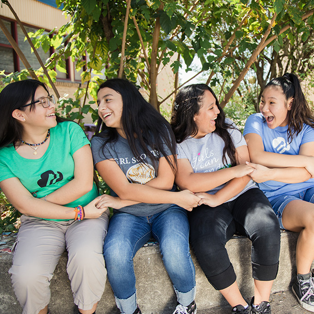 Photo of girls laughing with their arms crossed to hold hands. 