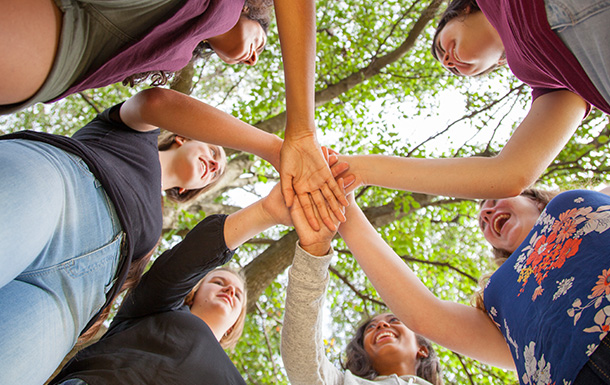 Photo of a circle of girls with their hands meeting in the center. 